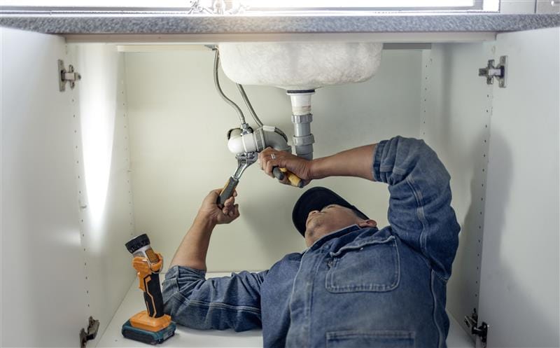 Plumber repairing pipes beneath a bathroom sink in Carmichael